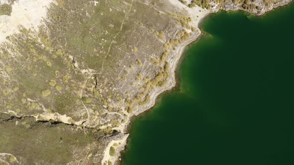 Bird eye perspective of a coastline with green colored ocean and a dry coutryside 