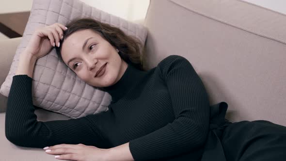 Young Lady Is Relaxing on Couch at Home Lying on Pillow and Smiling