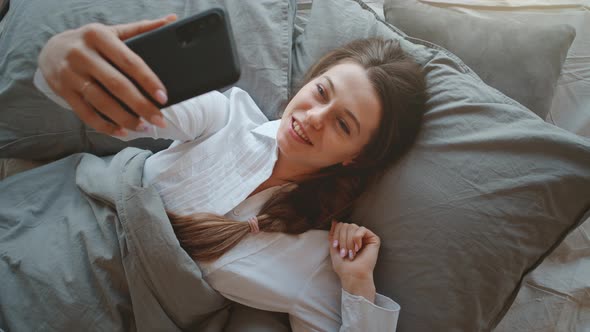 Relaxed Young Woman with Mobile Phone Lying in Bed at Home