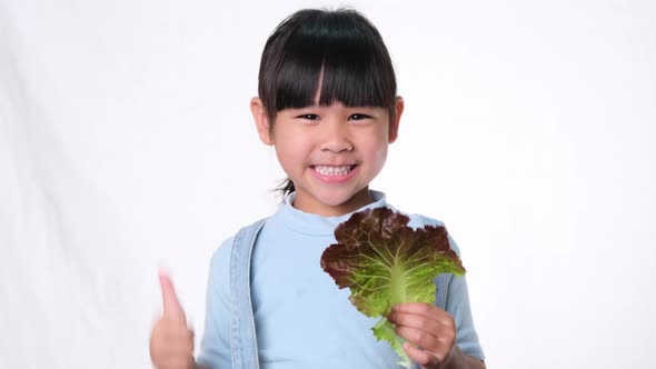 Happy little girl with fresh salad with showing thumbs up on white background in studio.