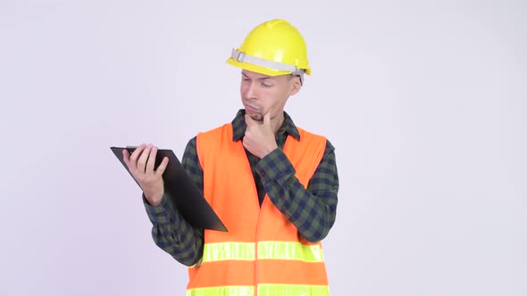 Studio Shot of Man Construction Worker Reading on Clipboard and Thinking