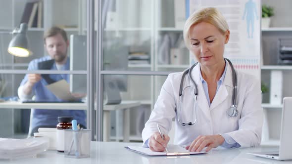 Female Doctor Taking Notes and Posing for Camera at Desk