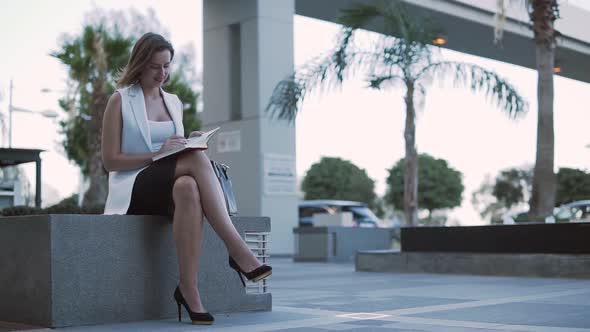 Smiling Businesswoman Checking Notes in Work Diary During Break Outdoors