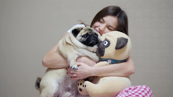 Beautiful Woman Hugs Pug Dog and Toy Pug at Home