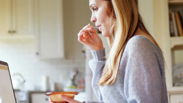 Woman using laptop while having breakfast