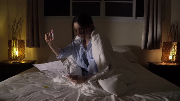 A Serious Young Lady Sits in a Bed and Reads Instruction for Express Covid Test Holding a Tube