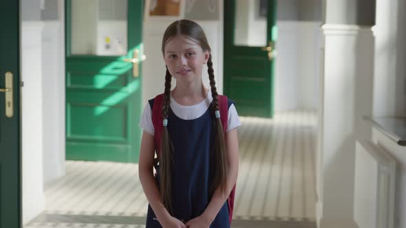 Portrait of Smiling Caucasian Schoolgirl Standing in School Corridor Wearing Schoolbag