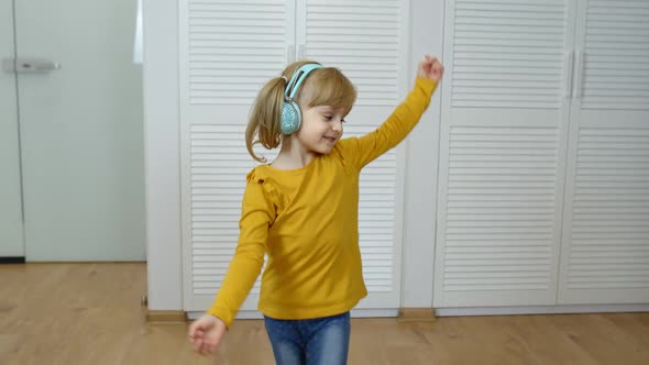 Little Child Girl Wearing Headphones Listening To Music and Funnily Dancing Near Wardrobe at Home