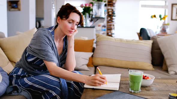 Young woman writing in note book on breakfast table and stroking baby 4k