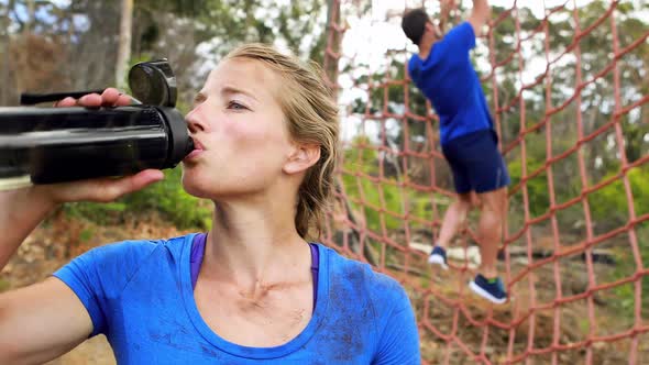 Fit woman drinking water after workout during obstacle course