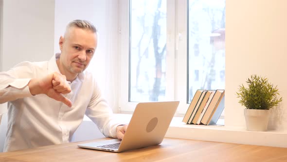 Thumbs Down by Middle Age Man while Working on Laptop