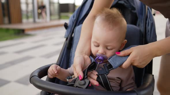 Mom Fastens the Baby in the Stroller for Safety on a Summer Day