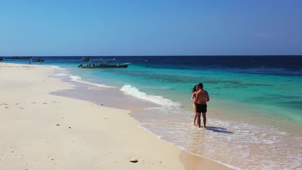 Family of two suntan on tranquil coastline beach holiday by blue water and white sandy background of