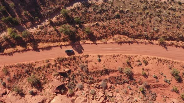 Dark SUV Drives On Dirt Road Crossing A Red Sand Desert On A Sunny Day