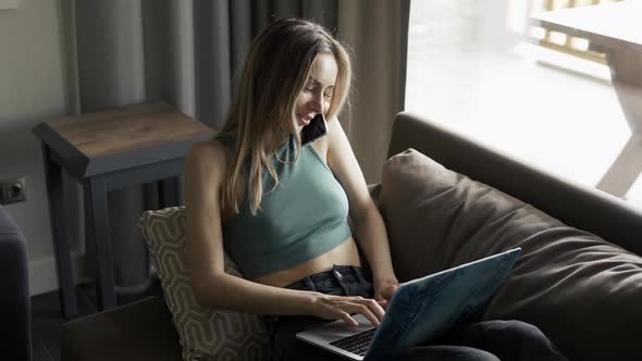 Blonde Woman Sitting on Sofa with Laptop and Talking By Smartphone