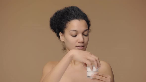 Beauty Portrait of Young African American Woman Twisting Off Jar of Cream and Dissatisfied with Its