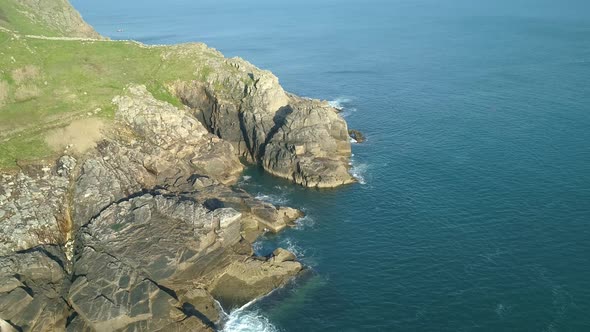 Aerial fly in of cornish coastline, waves gently lap against rocks
