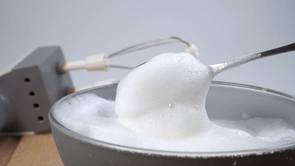 White froth of whipped milk in a full teaspoon flows down into a gray bowl