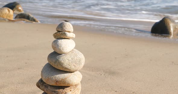 Woman hand put pebble in pyramid on the sea 