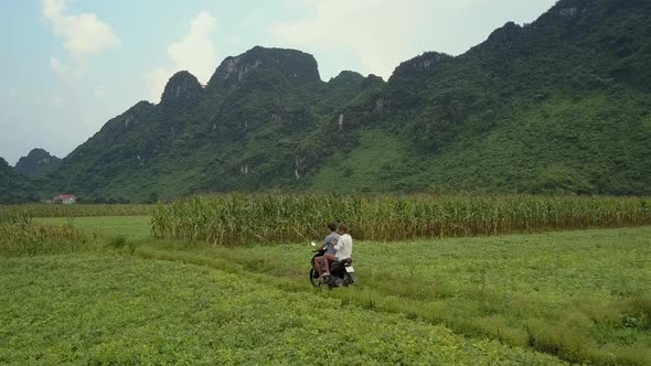 Tourists Ride Scooter Along Fields Against Hills Aerial View