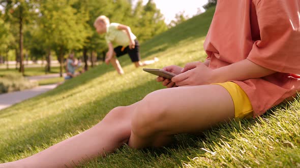 A Teenage Girl Holding a Tablet While Sitting on the Green Grass in a Park