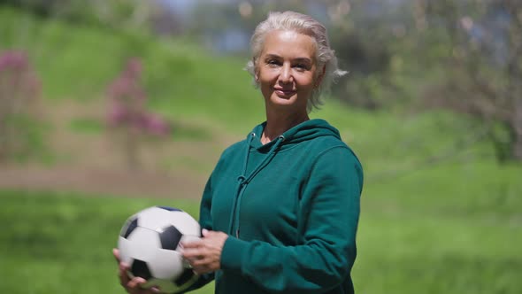 Charming Senior Sportswoman Playing with Ball Outdoors Looking at Camera Putting Hand on Hip