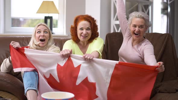 Joyful Female Hockey Fans Cheering Sitting in Living Room Indoors Watching Match on TV