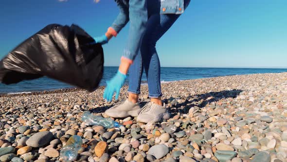 a female volunteer collects garbage in a black garbage bag.