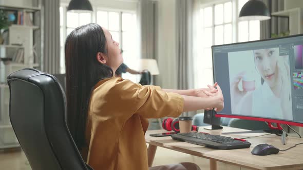 Asian Female Digital Editor Stretching While Works In Photo Editing Software On Computer