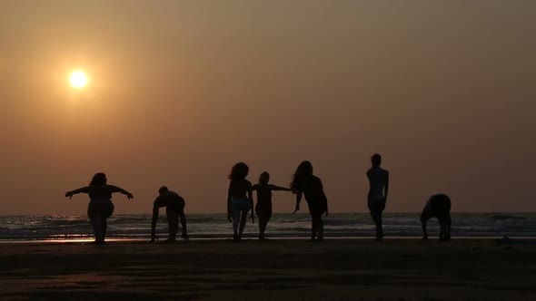 People stretching at a sandy beach in Goa at sunset.
