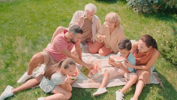 Multigenerational Family Eating Watermelon On Lawn