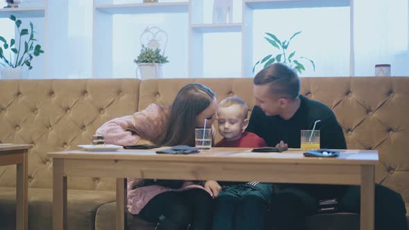 Happy Smiling Parents Hug and Kiss Child in Restaurant