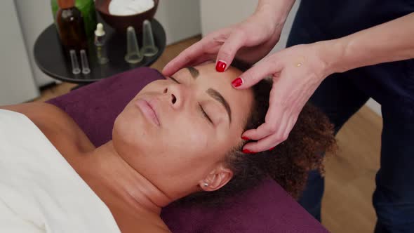 Masseuse Applying Facial Lotion Massaging Woman's Forehead Indoors