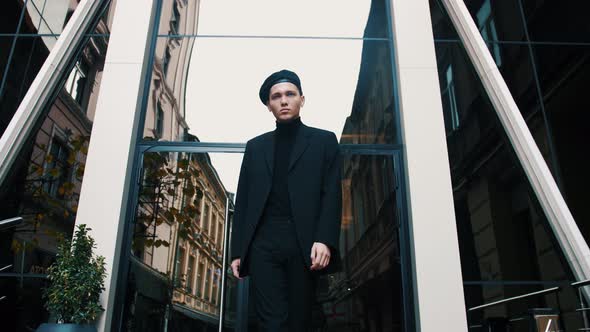 Confident and Handsome Young Businessman with Beret Walking Down Modern City Street and Looking Away