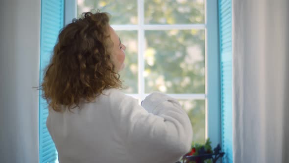 Happy Woman in Bathrobe Stretching at Window in Morning