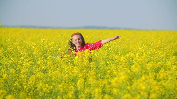 Girl Walks Across the Field with Canola Flowers