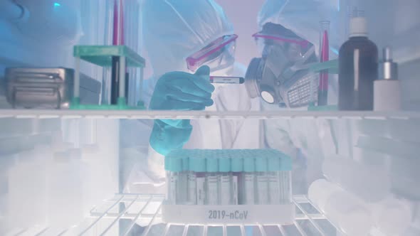 Scientists in Protective Uniform Examine Sample in Laboratory Fridge