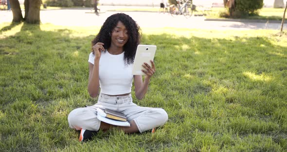 Joyful Black Woman Listening to Music on Tablet in Park in Sunny Day