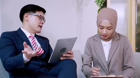 Two male and female hijab business colleagues using digital tablet, notepad and discussing project