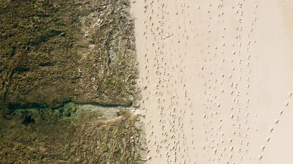 Drone Following Above White Sandy Beach with Foot Traces Near Coastline with Reef
