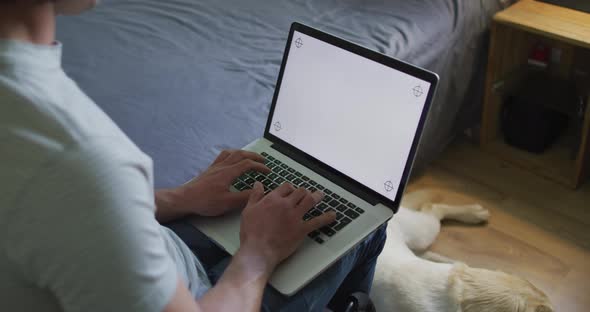 Caucasian man using laptop in bedroom with pet dog