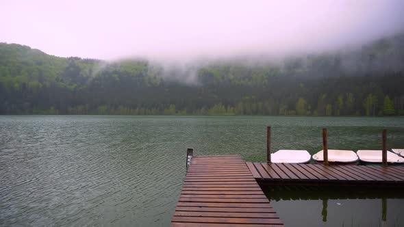 Boats floating on the lake close to the wooden pier. Smooth calm surface of mountain lake