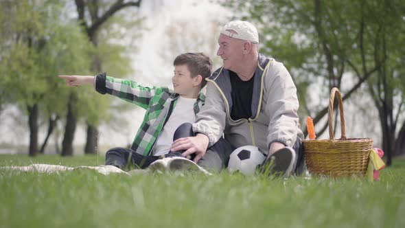 Old Man Sitting with His Grandson on the Blanket in the Park