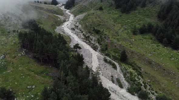 A Small Turbulent Mountain River Flows Over Stones in a Misty Gorge in Cloudy Weather Surrounded By