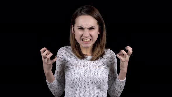 The Young Woman Shows Emotions of Anger on His Face. Girl Grins Teeth and Frowns Eyebrows on a Black