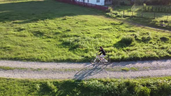 Aerial footage of a male ridding his bike on a country road on a sunny summer day