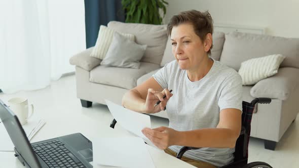 Senior Female Freelancer Working at Home Writing Writing Notes While Sitting in a Wheelchair