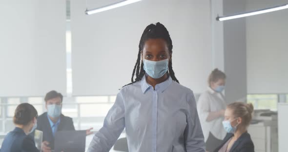 African American Woman Standing in Office in Front of Team and Wear Facial Mask