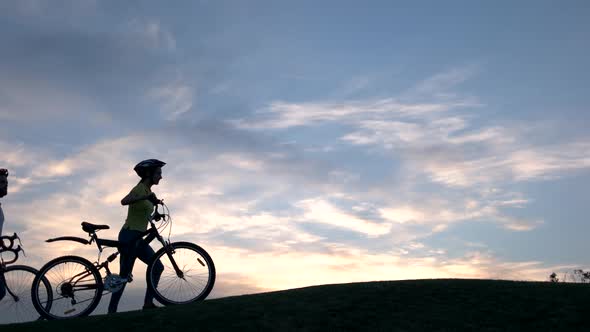 Young Cyclists Walking on Hill at Sunset