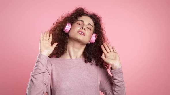 Beautiful Woman with Curly Hair Dancing with Headphones on Pink Studio